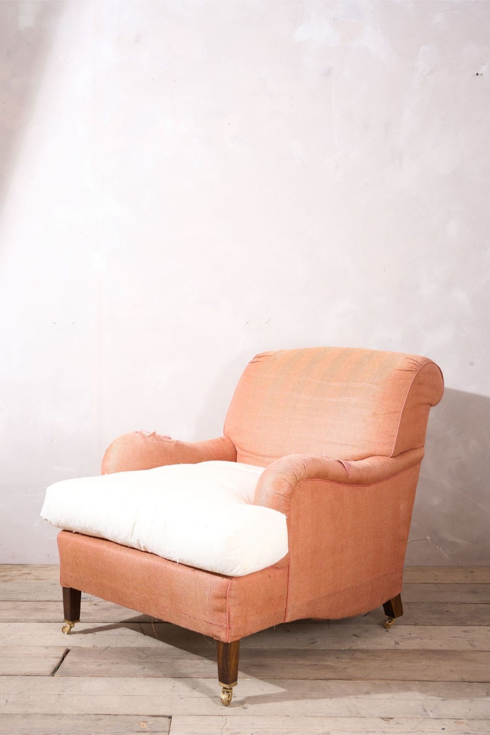 A twentieth-century Bridgewater style armchair upholstered in textured terracotta fabric featuring a white seat cushion and square wooden legs with brass castors.