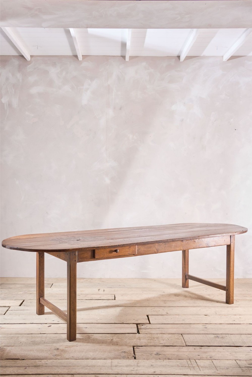 An eighteenth-century French provincial dining table made of solid elm with a large oval top, side frieze drawer, and square legs joined by end stretchers.