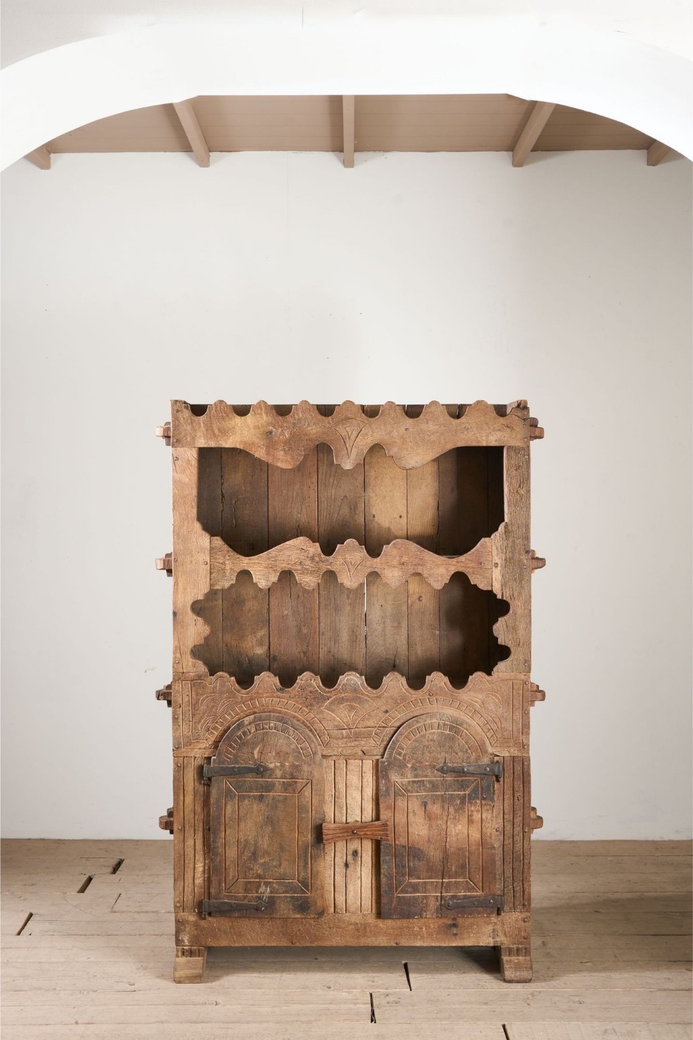 An 18th-century Spanish Pyrenean folk art carved oak cupboard featuring scalloped open upper shelves and a two-door lower section with wrought iron hardware.