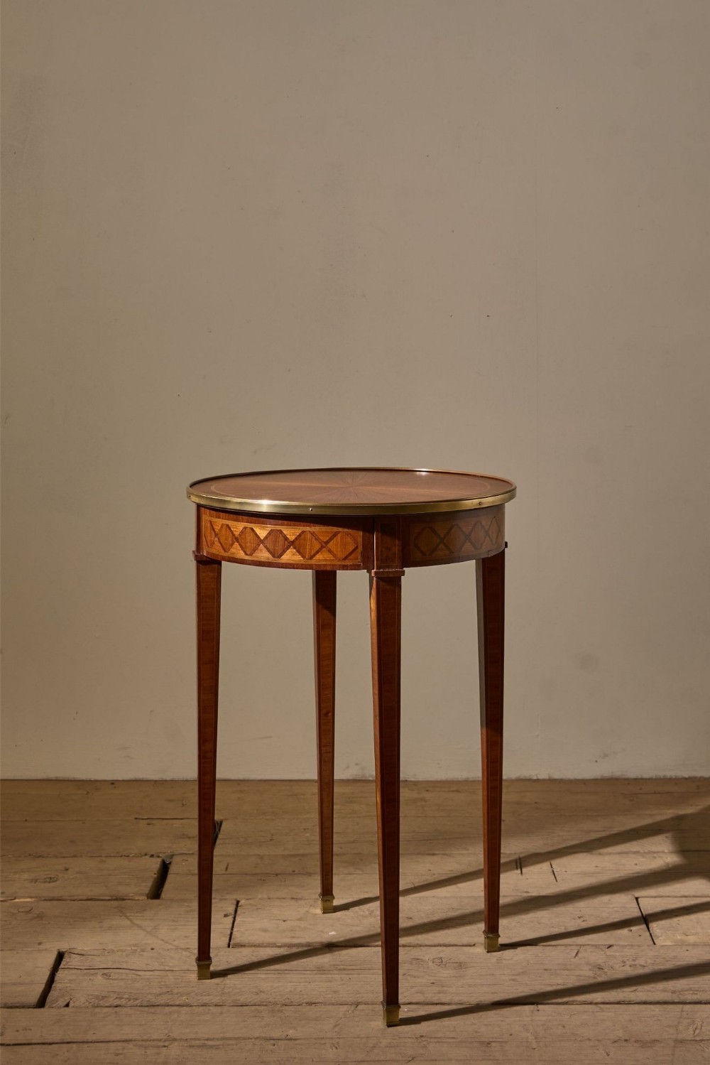 A circular French mahogany gueridon table featuring a brass rim, geometric parquetry inlay around the apron, and four square tapered legs ending in brass feet.