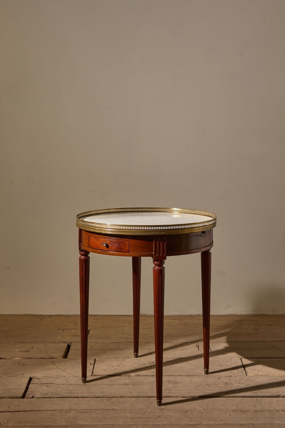 A circular early 20th-century mahogany gueridon side table with an inset white marble top, pierced brass gallery, and fluted tapered legs.