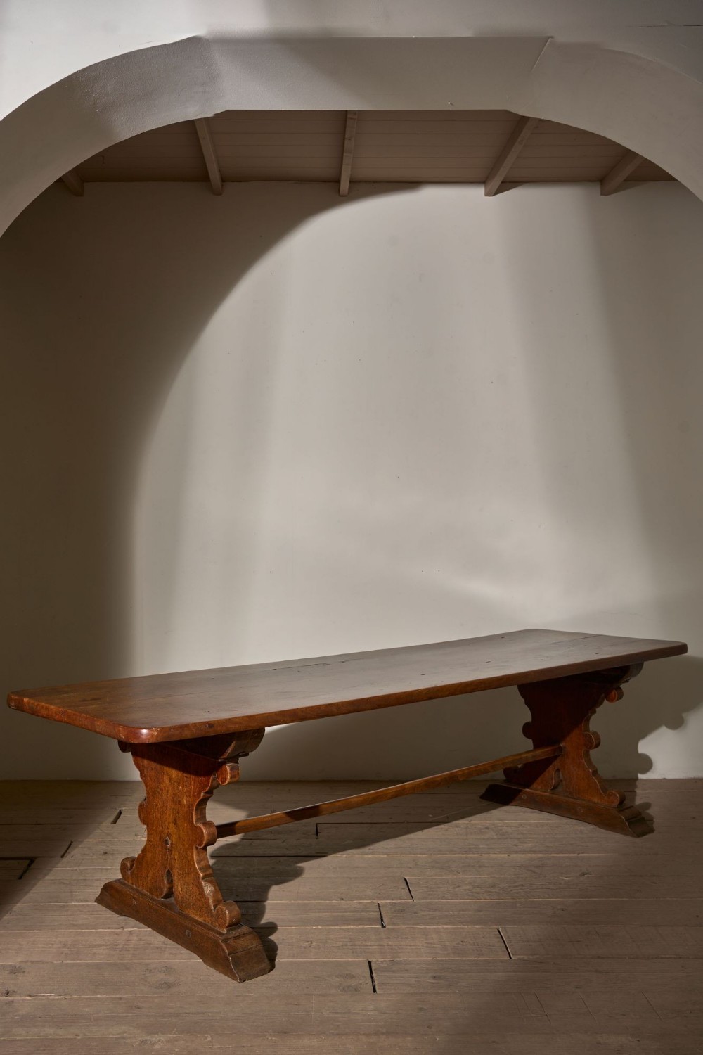 A 19th-century oak refectory table featuring a two-plank top resting on shaped trestle end supports connected by a low central stretcher.