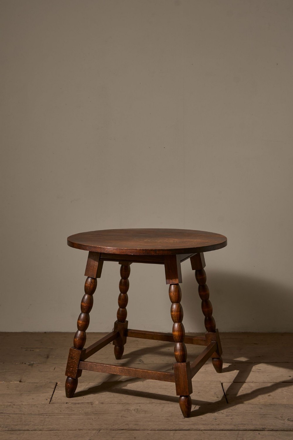 A circular mid-20th-century dark oak side table featuring four bobbin-turned legs joined by a low square stretcher base.