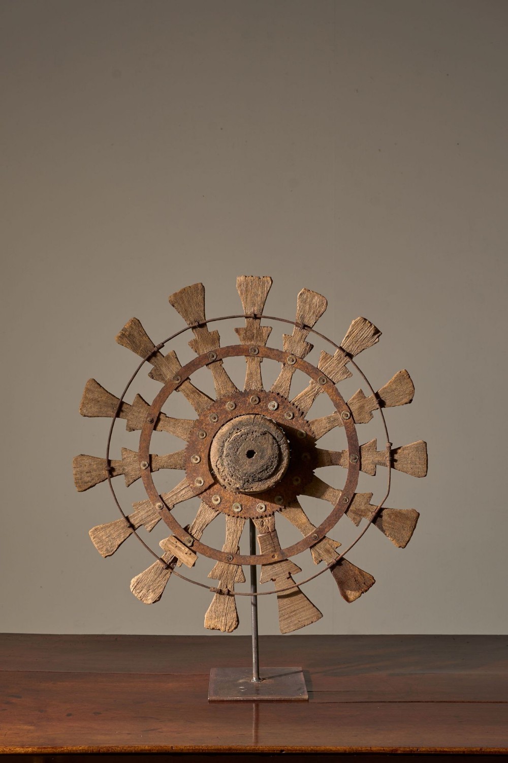 A 19th-century carved wooden Indian silk spinning wheel with radiating spokes and iron rims, mounted upright on a dark metal museum stand.