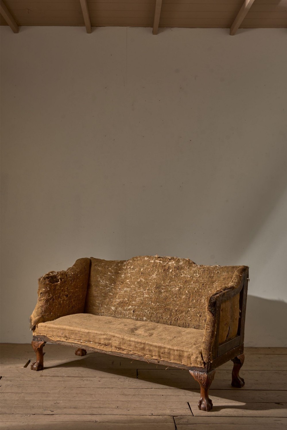 A 19th-century mahogany campaign sofa frame with deconstructed hessian upholstery and carved ball and claw feet.