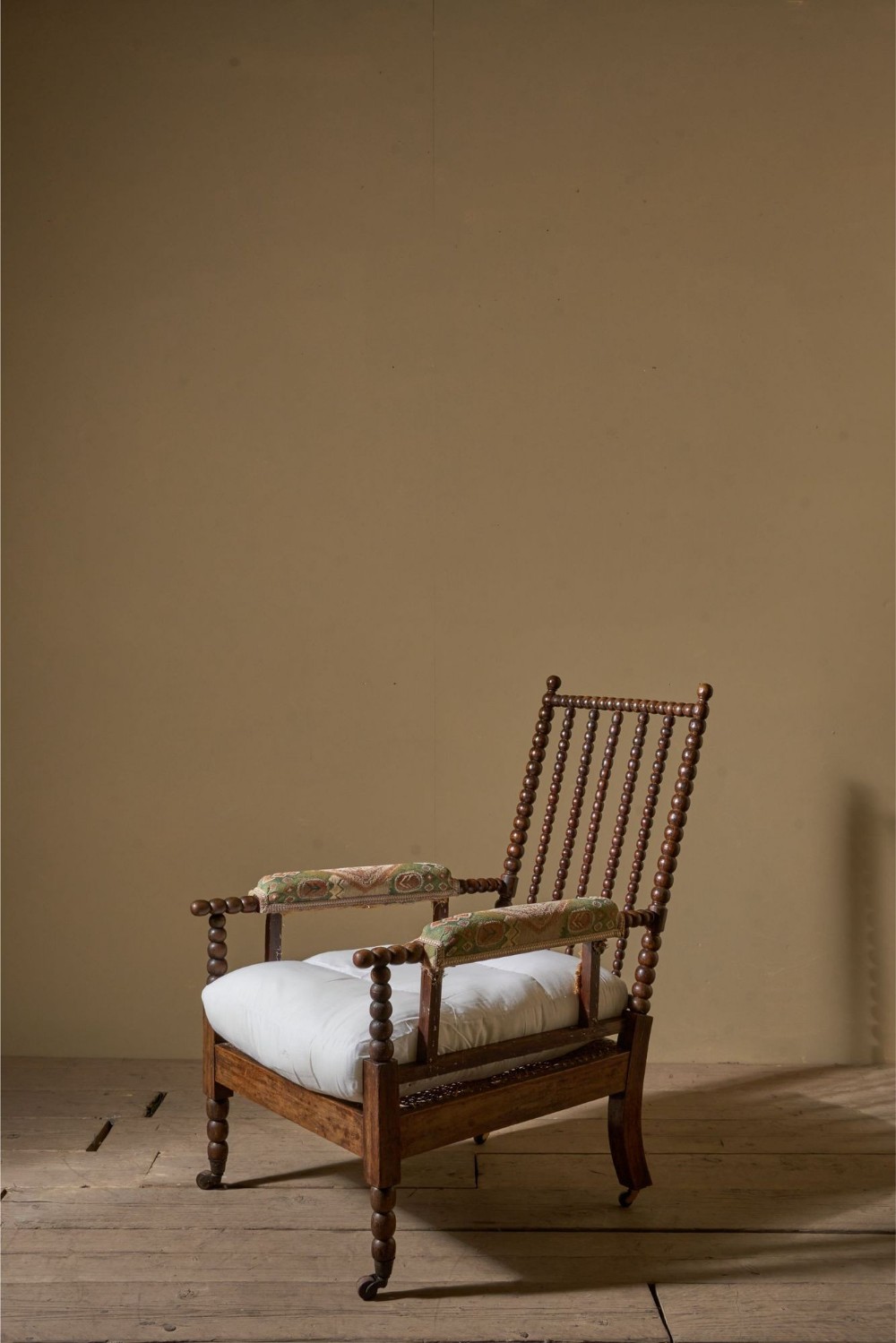 A 19th-century bobbin-turned armchair featuring simulated rosewood timber, patterned armrest upholstery, a white seat cushion, and brass castors.