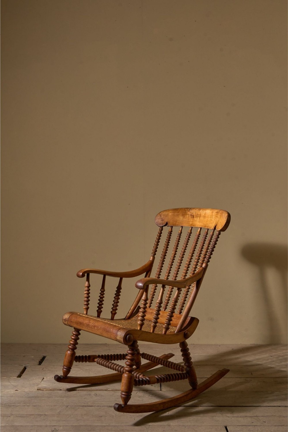 A nineteenth-century wooden rocking chair featuring bobbin-turned spindles, curved armrests, and a woven cane seat.