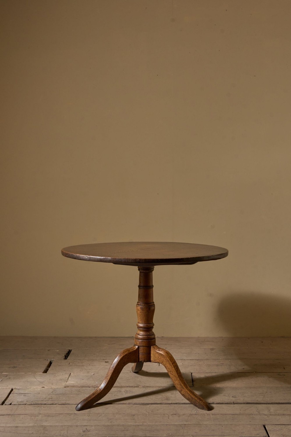 An 18th-century oak tilt-top table with a circular surface, a turned central pedestal, and three down-swept tripod legs.