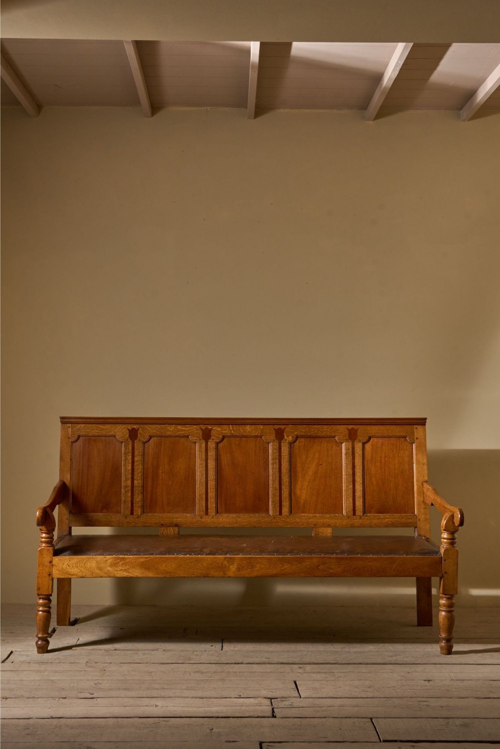 A Georgian oak hall bench featuring a high panelled backrest with tulip motif inlays, curved armrests, a leather seat, and turned front legs.