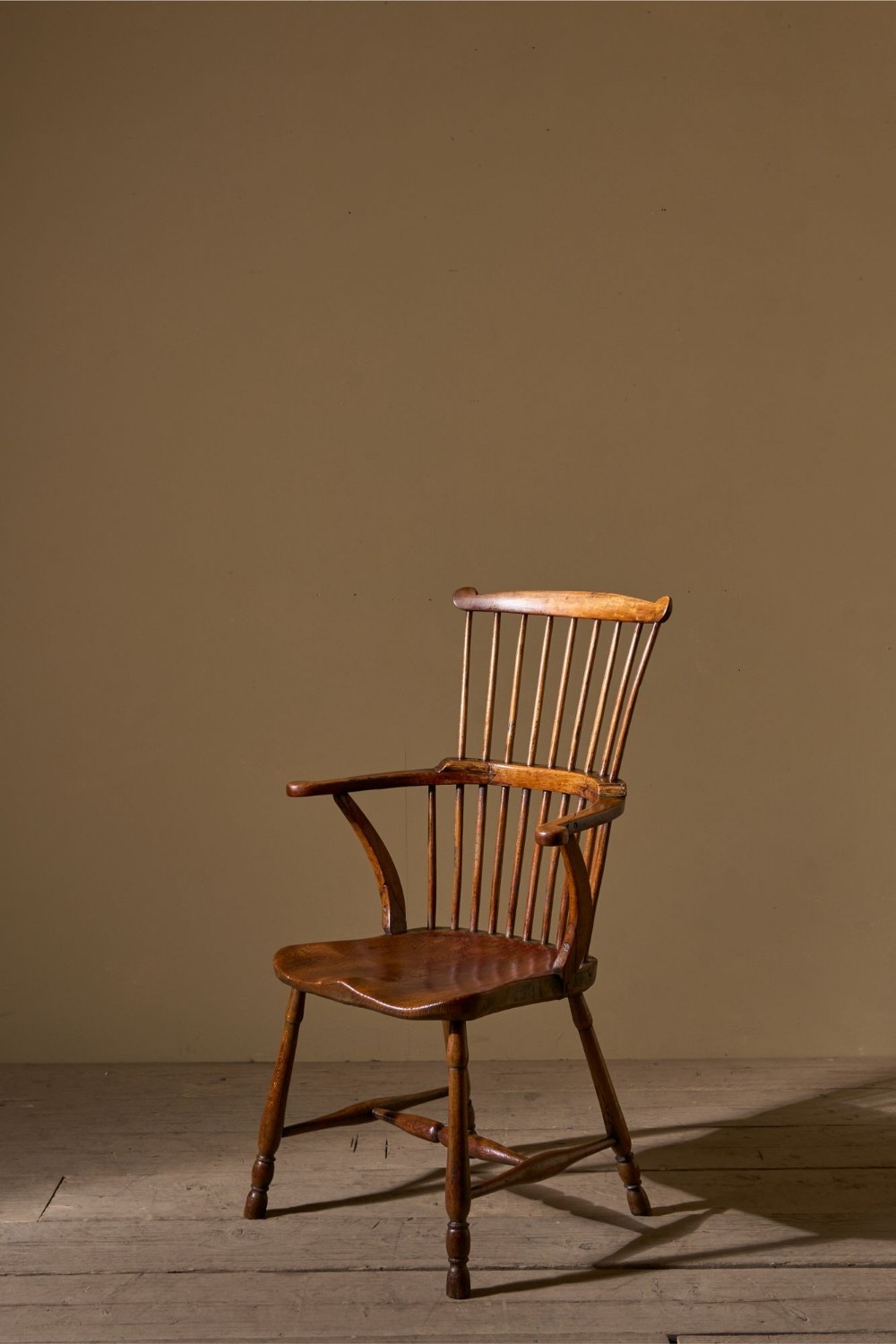 An 18th-century comb back Windsor armchair constructed from ash and elm with turned spindles, shaped armrests, turned legs, and an H-stretcher.