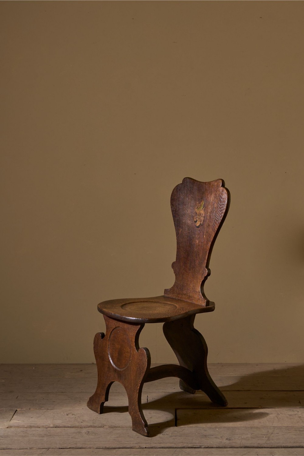 An eighteenth-century dark oak hall chair featuring a shaped shield back with a faint painted crest and a circular dished seat.