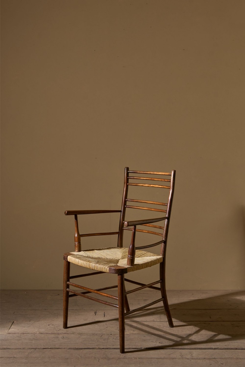 An Arts and Crafts dark oak armchair featuring a ladder back design, turned arm supports, and a natural woven rush seat.