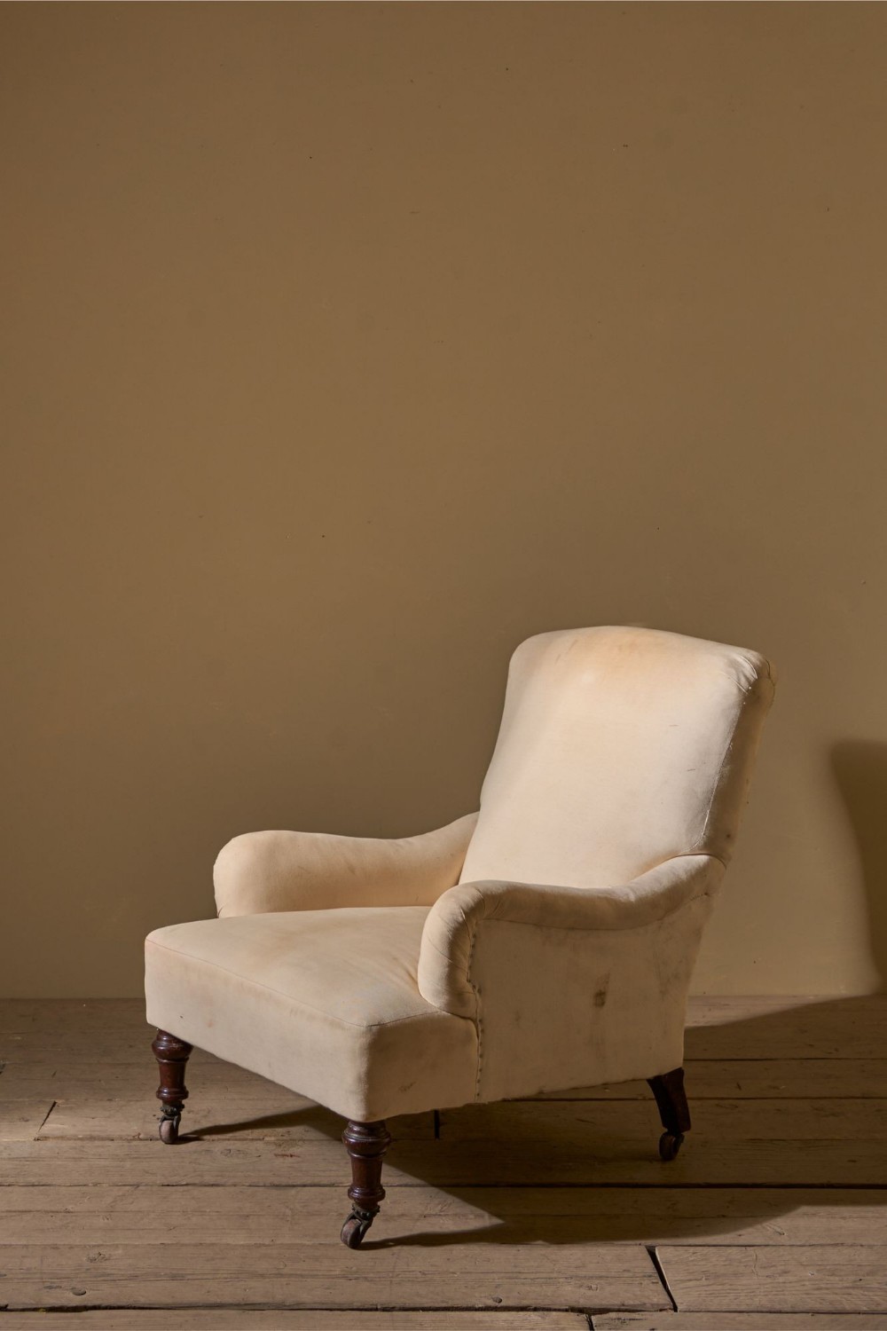 A 19th-century Bridgewater-style armchair upholstered in light cream fabric with turned mahogany front legs on castors.