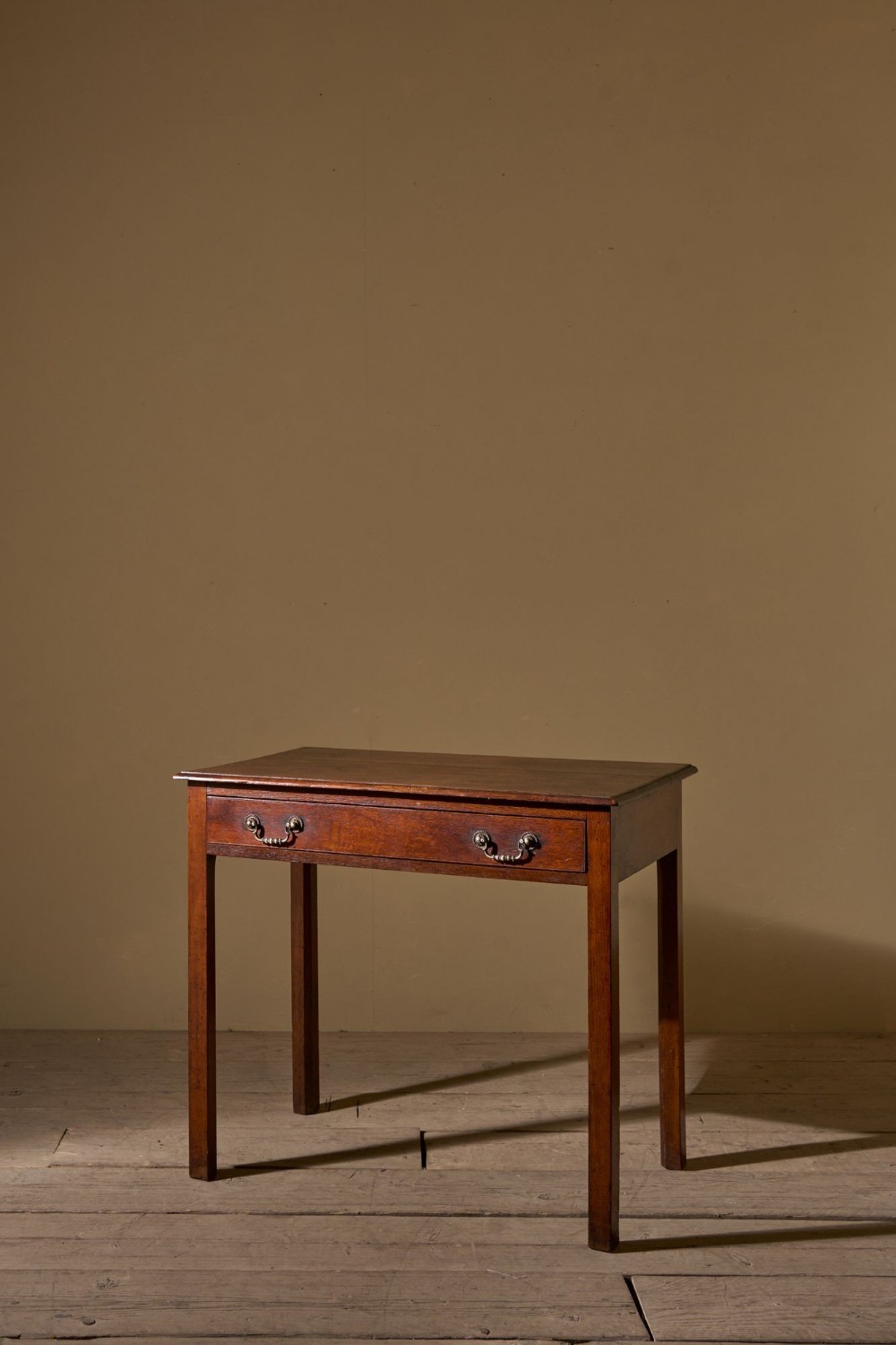 An 18th-century dark oak side table featuring a full-width drawer with dual brass handles and slender square legs.