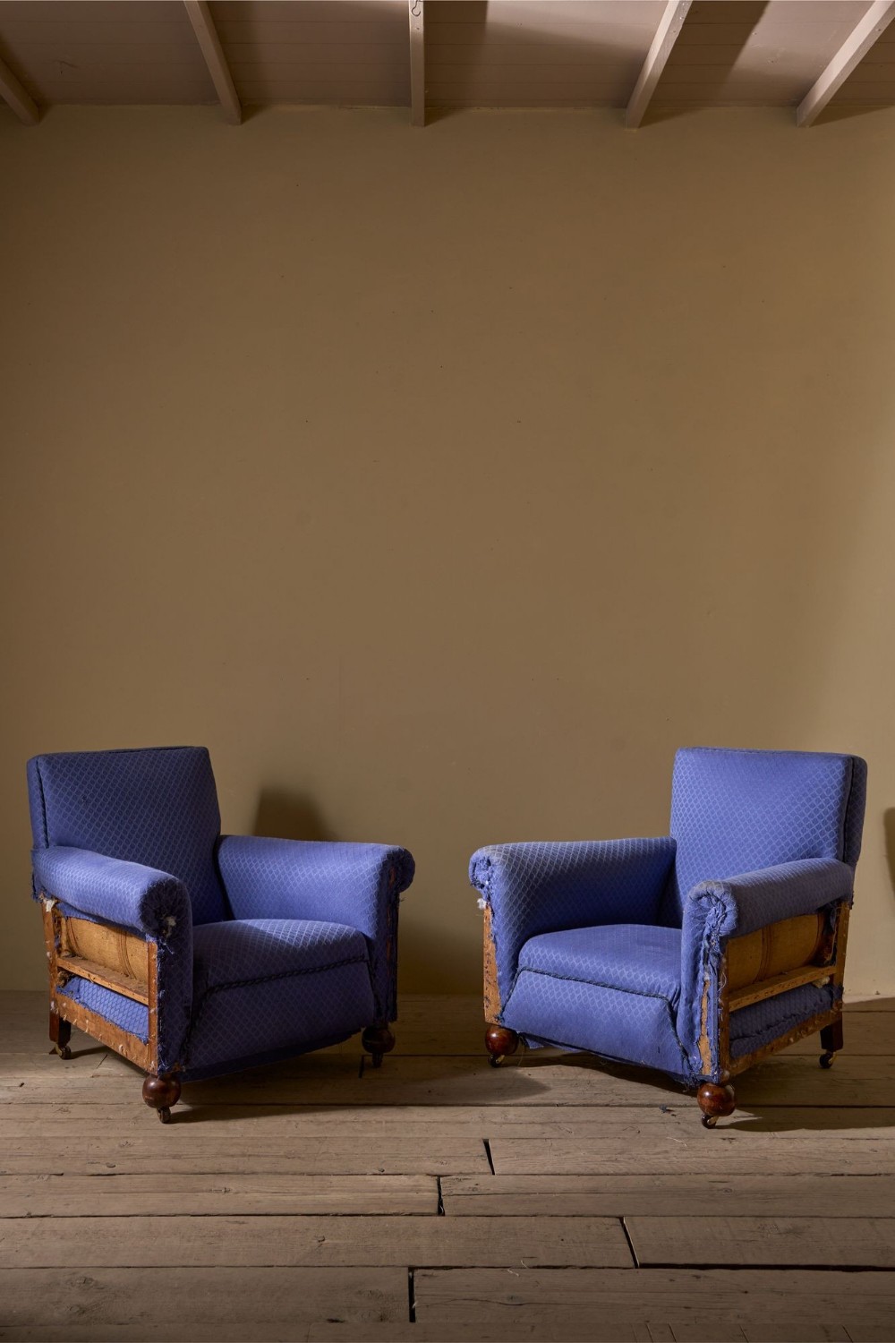 A pair of vintage Art Deco club armchairs upholstered in blue patterned fabric featuring turned wooden feet with castors.