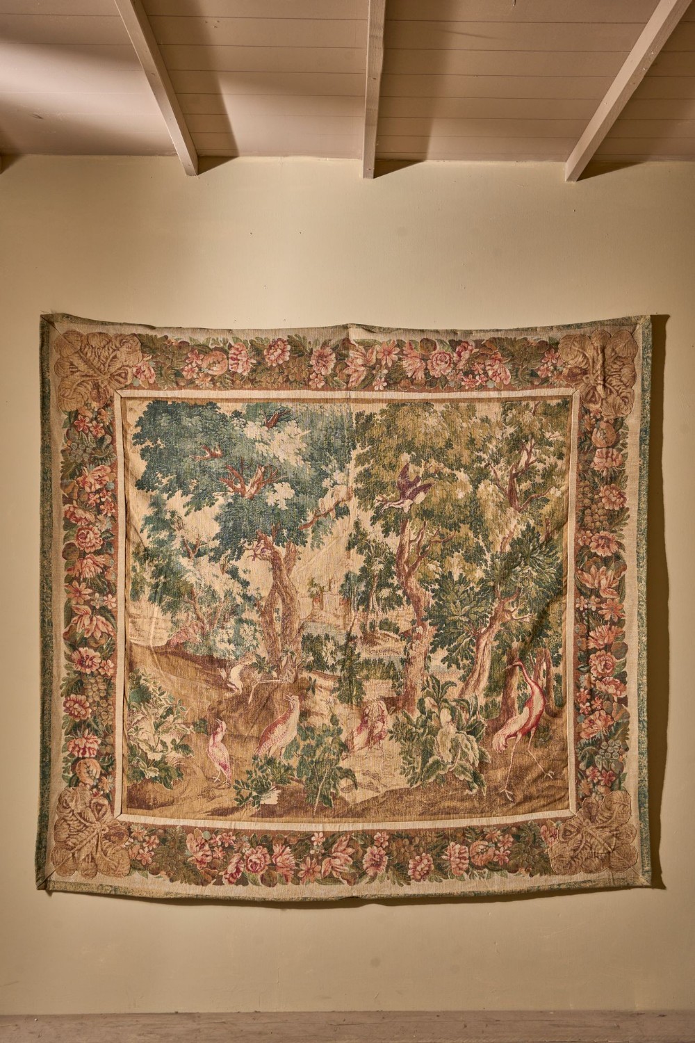 A large 19th-century woven wall tapestry depicting a woodland landscape with birds, enclosed within a wide floral border.