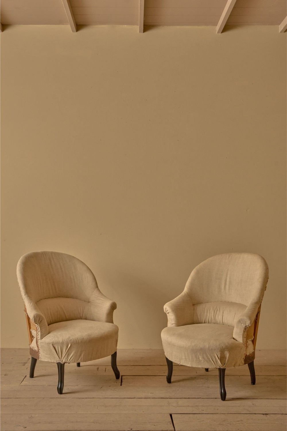 A pair of antique French Napoleon III tub chairs upholstered in neutral calico with dark turned wooden legs.