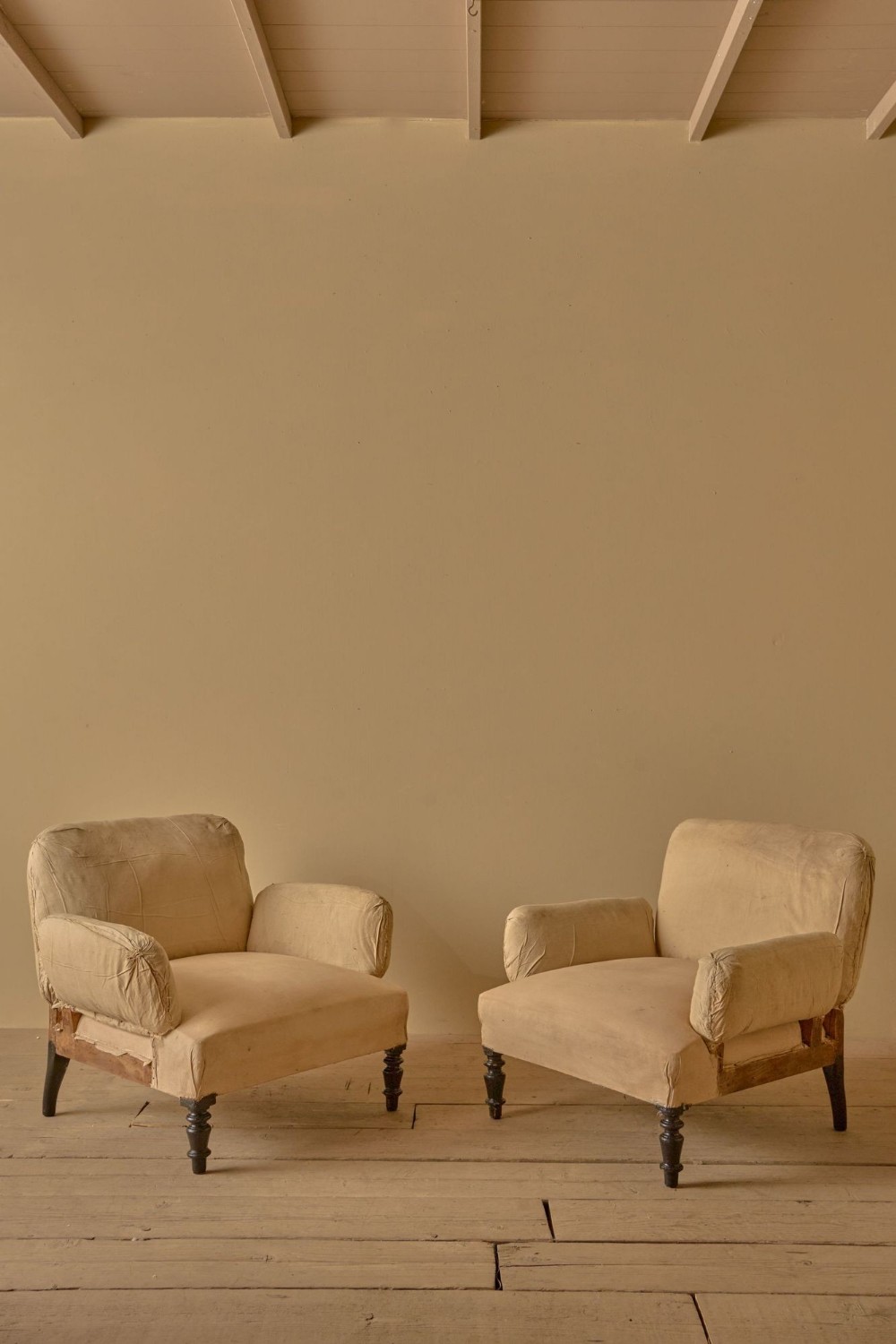 A pair of 19th-century French Napoleon III armchairs upholstered in neutral calico fabric with padded pillow arms and dark turned front legs.