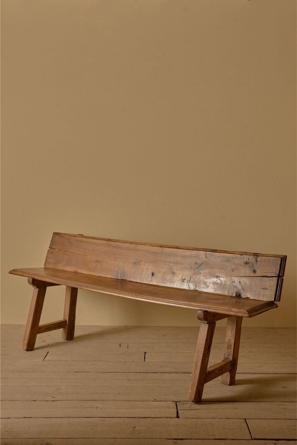 An 18th-century solid walnut hall bench with a single-plank backrest, angled seat edge, and splayed legs with side stretchers.