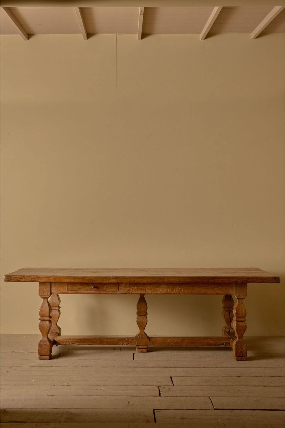 An 18th-century solid chestnut refectory dining table featuring turned baluster legs, a low perimeter stretcher, and a single frieze drawer.