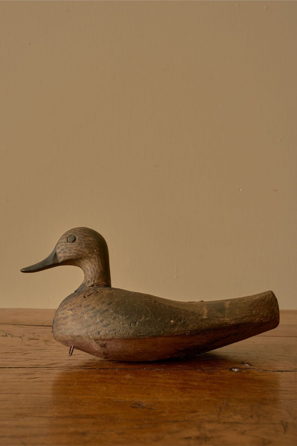 A hand-carved early 20th-century wooden decoy duck featuring distressed brown painted plumage detail on a timber surface.