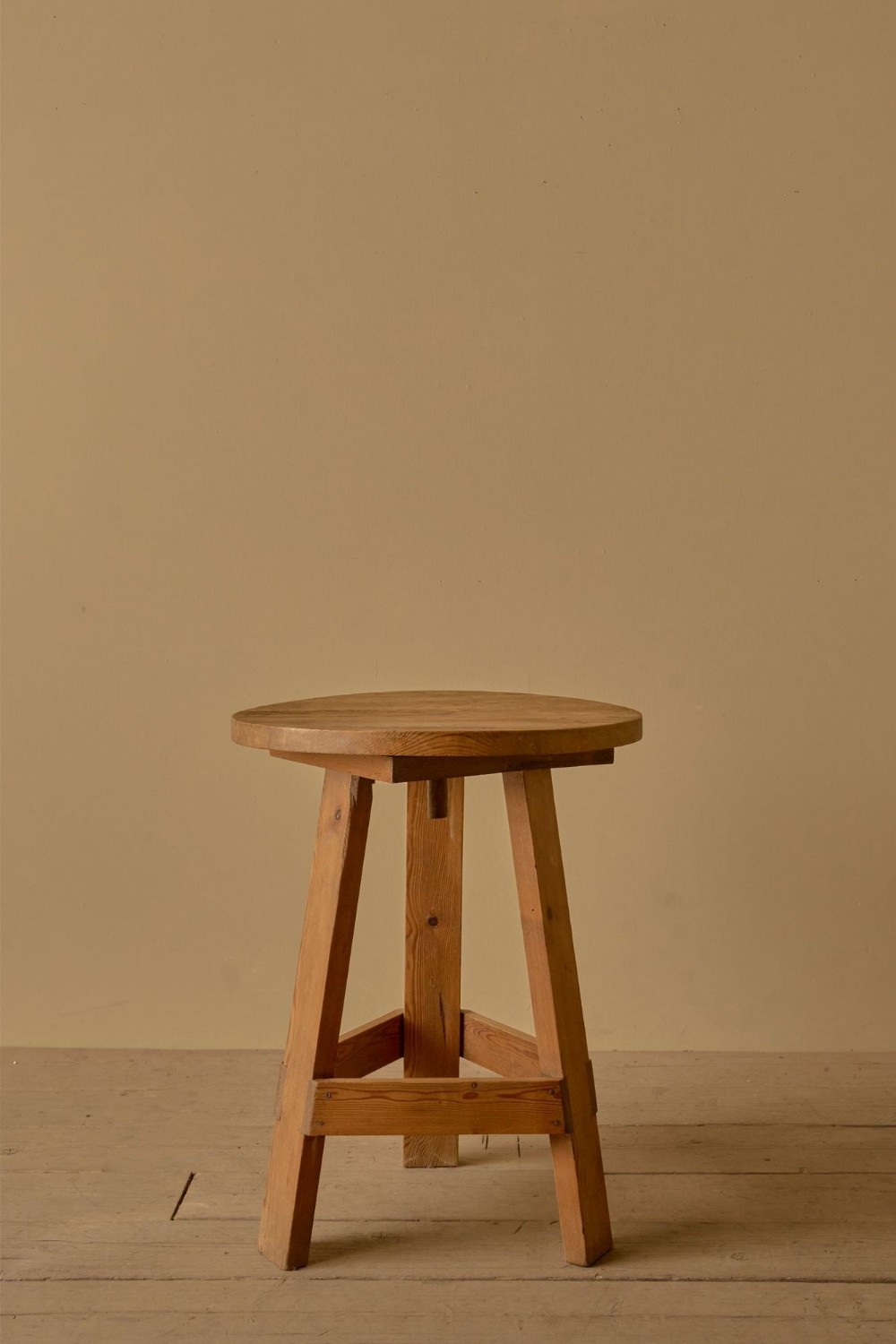 An early 20th-century pine sculptors stand with a circular top, splayed legs, and lower cross-bracing.