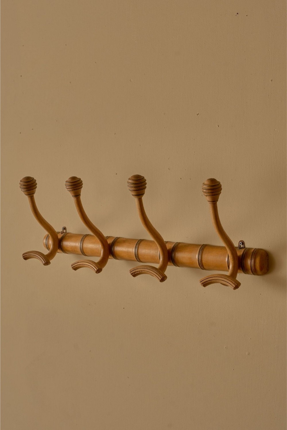A wall-mounted 19th-century French faux bamboo coat rack with four carved wooden double hooks set against a neutral wall.