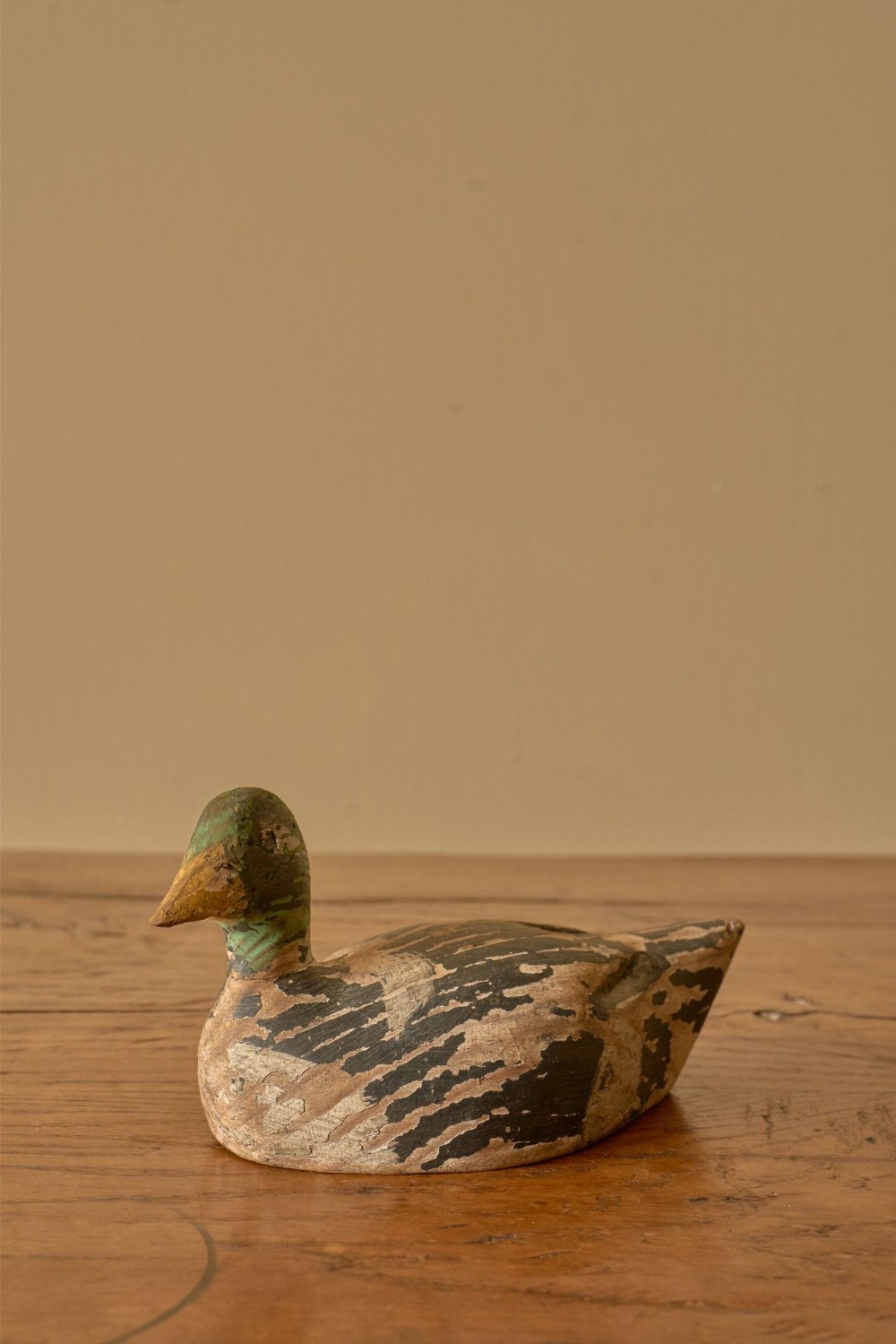 An early twentieth-century hand-carved wooden decoy duck featuring a green head, carved bill, and a distressed painted finish on its body.