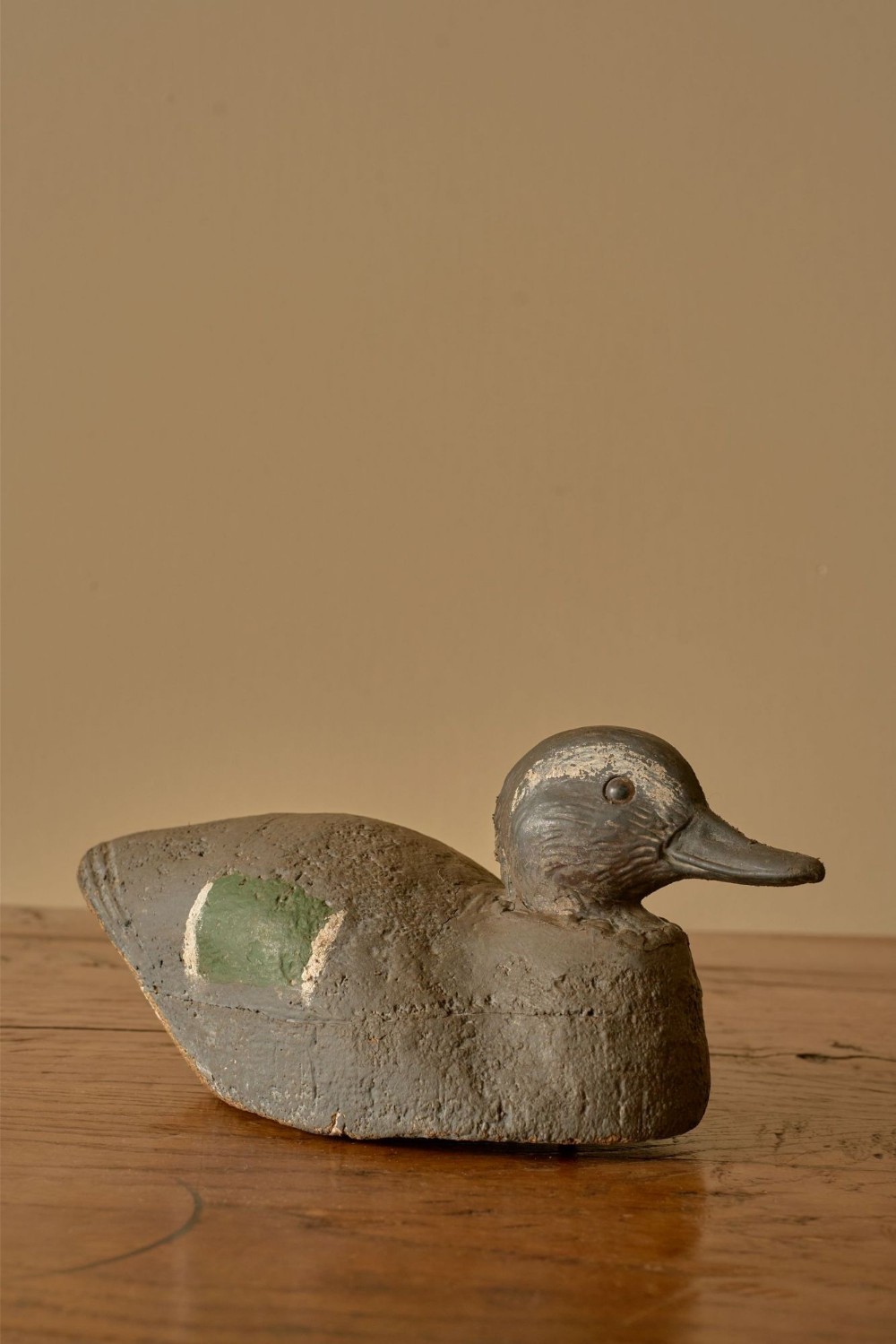 A carved wooden decoy duck with a grey painted body, textured finish, and a green painted speculum patch on its side.