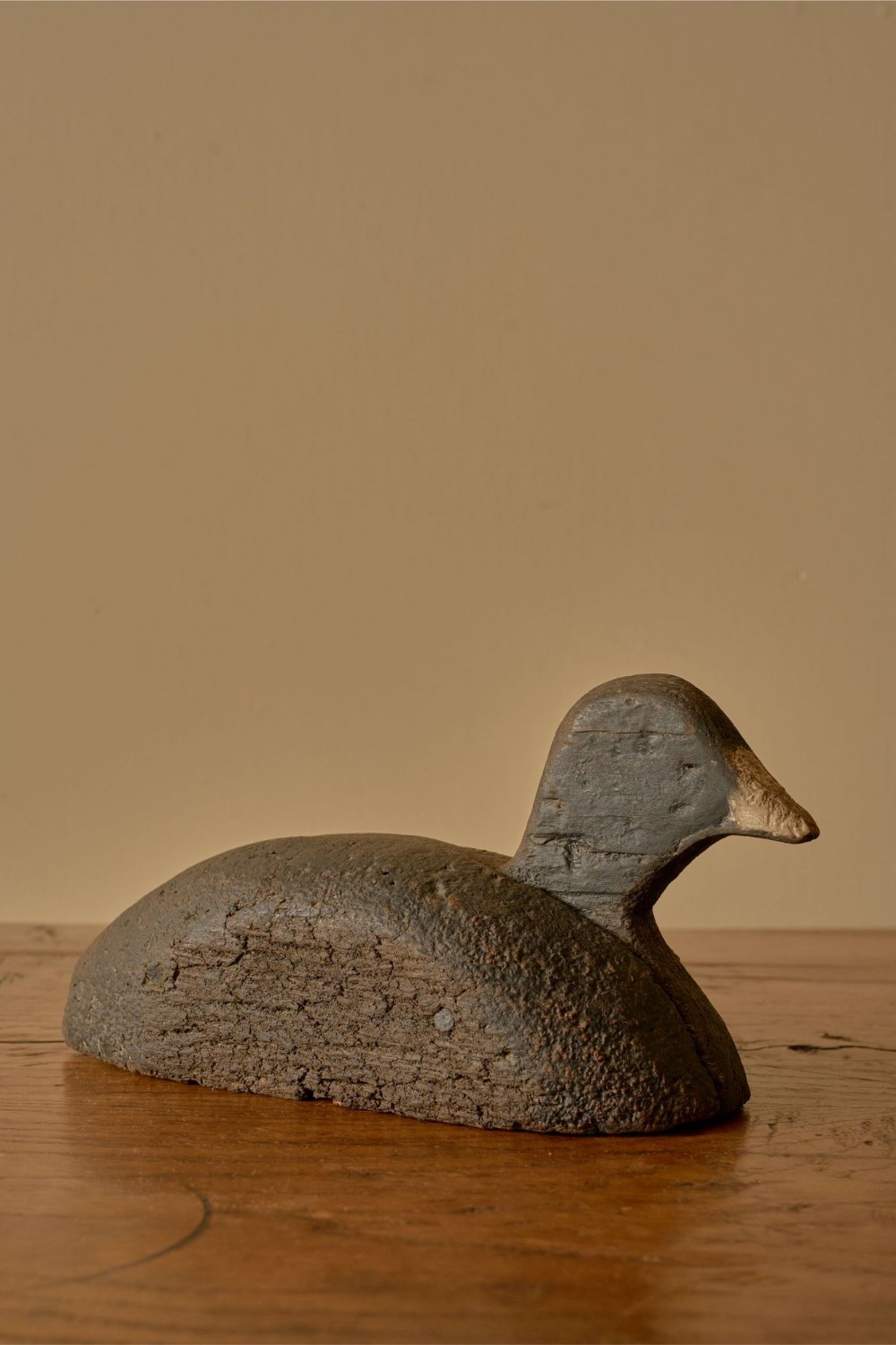 A carved wooden decoy duck with a weathered dark brown finish and tapered beak.