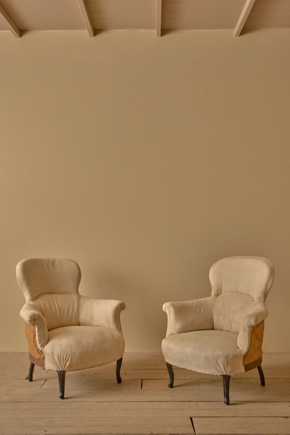 A pair of antique Napoleon III armchairs upholstered in cream calico, featuring spoon-shaped backs, scrolled armrests, and dark cabriole front legs.