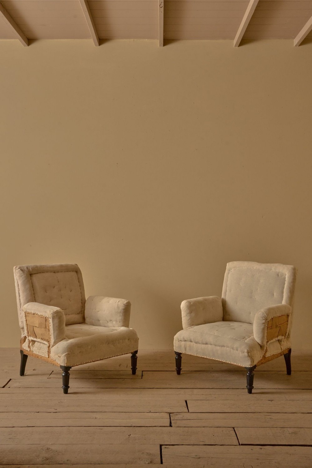 A pair of nineteenth-century French Napoleon III high-backed armchairs upholstered in off-white calico with pillow arms and dark turned wooden front legs.