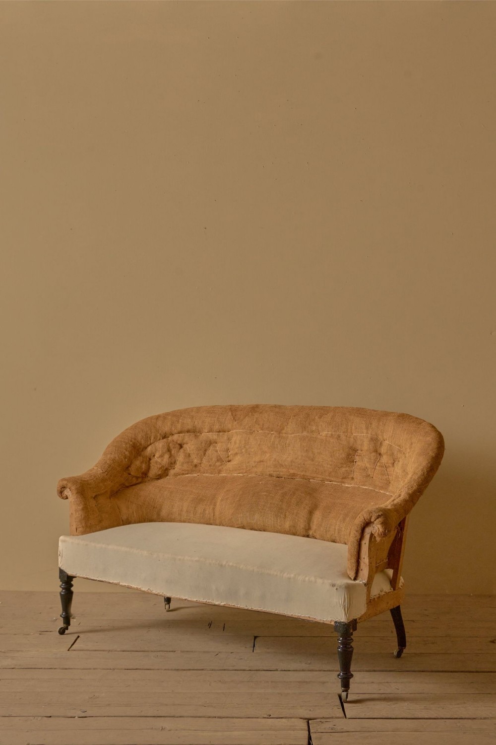 A nineteenth-century French Napoleon III sofa with a curved back, hessian covering, and turned dark timber legs on castors.