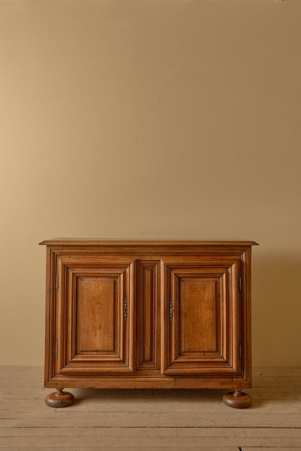 An 18th-century Dutch oak cupboard featuring two fielded panel doors, central moulded detail, and turned bun feet against a neutral wall.