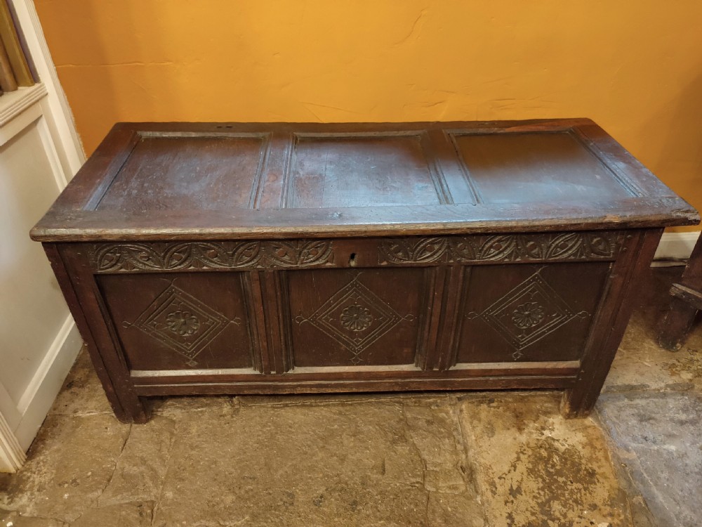A dark oak 17th-century coffer featuring three carved front panels with diamond lozenges and a carved top frieze below a panelled hinged lid.