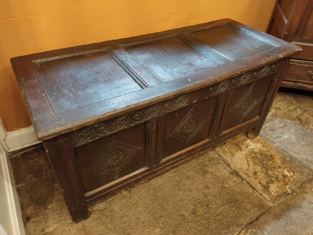 A dark oak 17th-century coffer featuring three carved front panels with diamond lozenges and a carved top frieze below a panelled hinged lid. View II