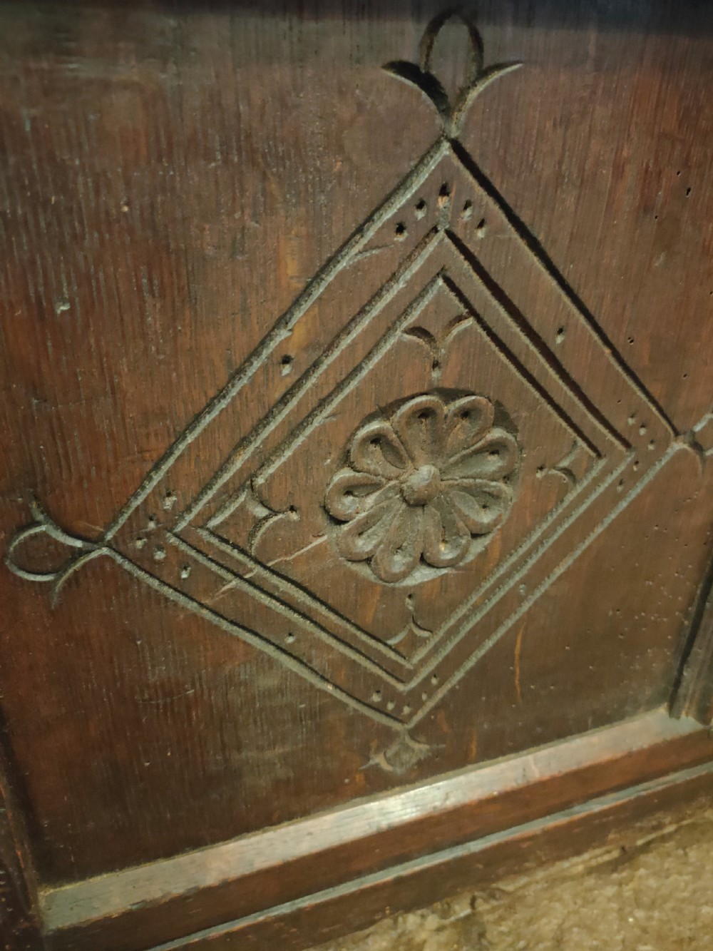A dark oak 17th-century coffer featuring three carved front panels with diamond lozenges and a carved top frieze below a panelled hinged lid. View V