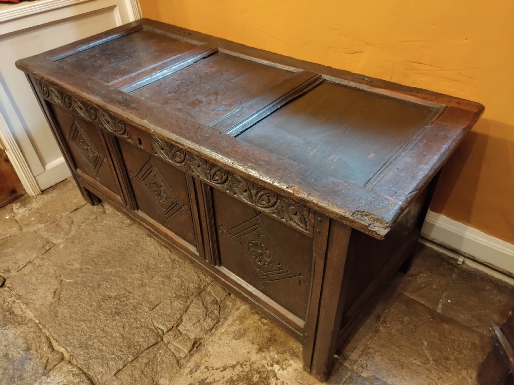 A dark oak 17th-century coffer featuring three carved front panels with diamond lozenges and a carved top frieze below a panelled hinged lid. View VI