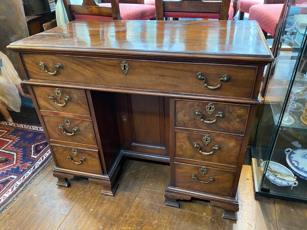 An eighteenth century Georgian mahogany kneehole desk featuring multiple drawers with brass handles, a central recessed cupboard, and bracket feet.