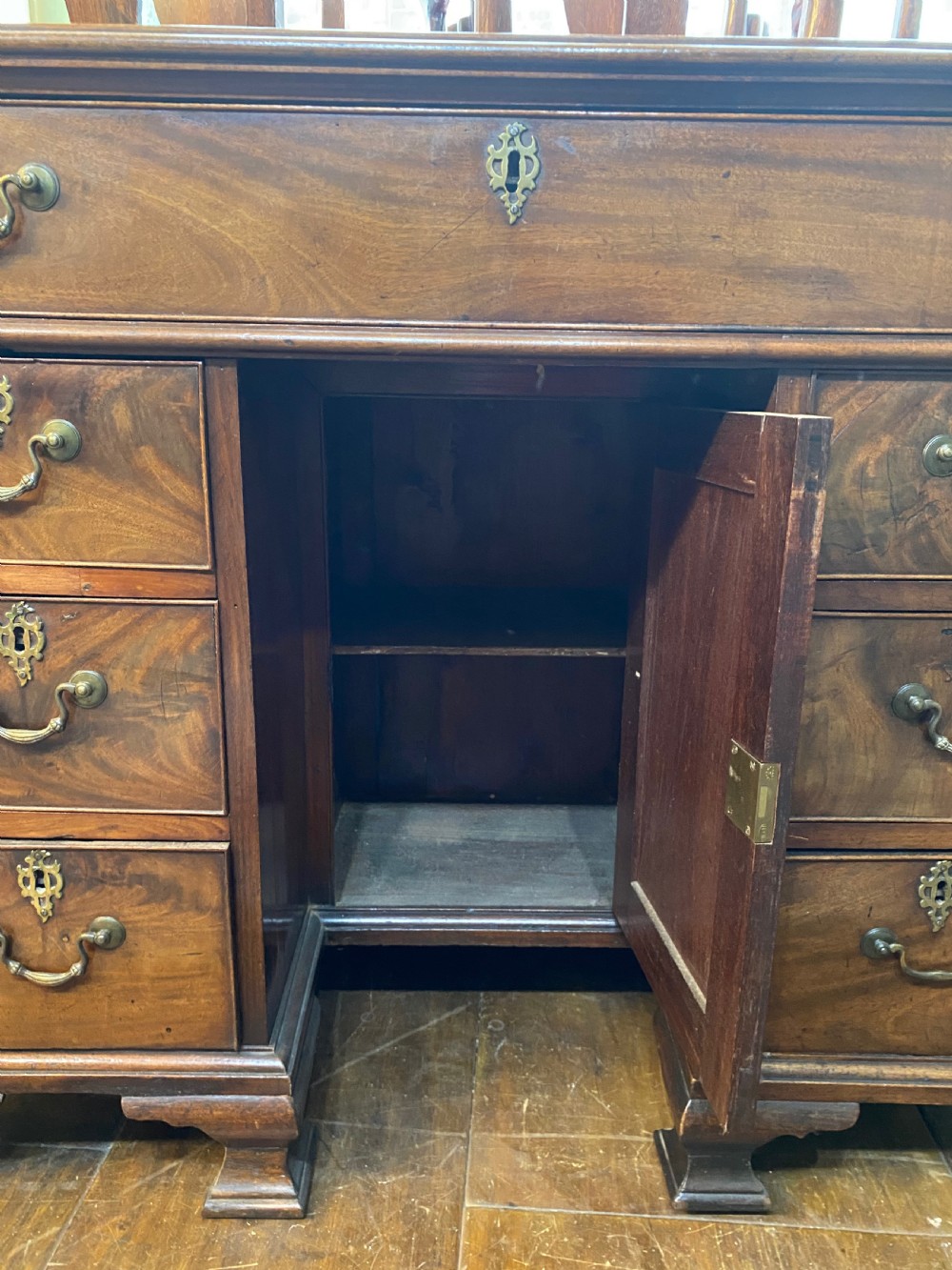An eighteenth century Georgian mahogany kneehole desk featuring multiple drawers with brass handles, a central recessed cupboard, and bracket feet. View IV