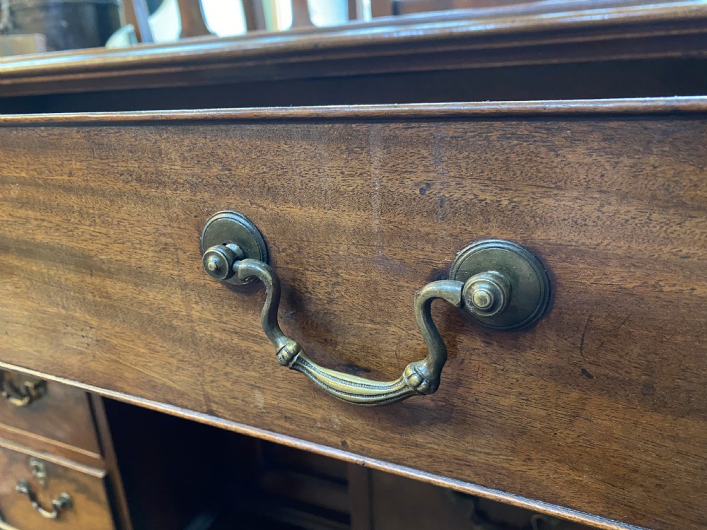 An eighteenth century Georgian mahogany kneehole desk featuring multiple drawers with brass handles, a central recessed cupboard, and bracket feet. View V