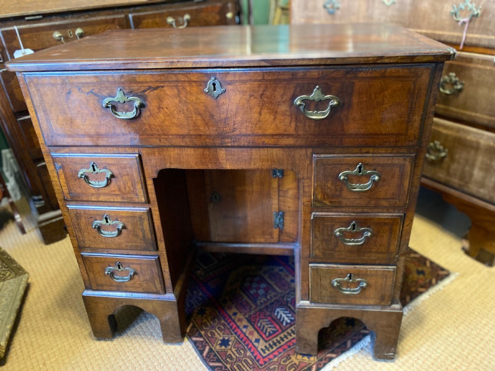 Mid 18th-century walnut kneehole secretaire desk featuring crossbanded drawer fronts, brass drop handles, a central recessed cupboard, and bracket feet.