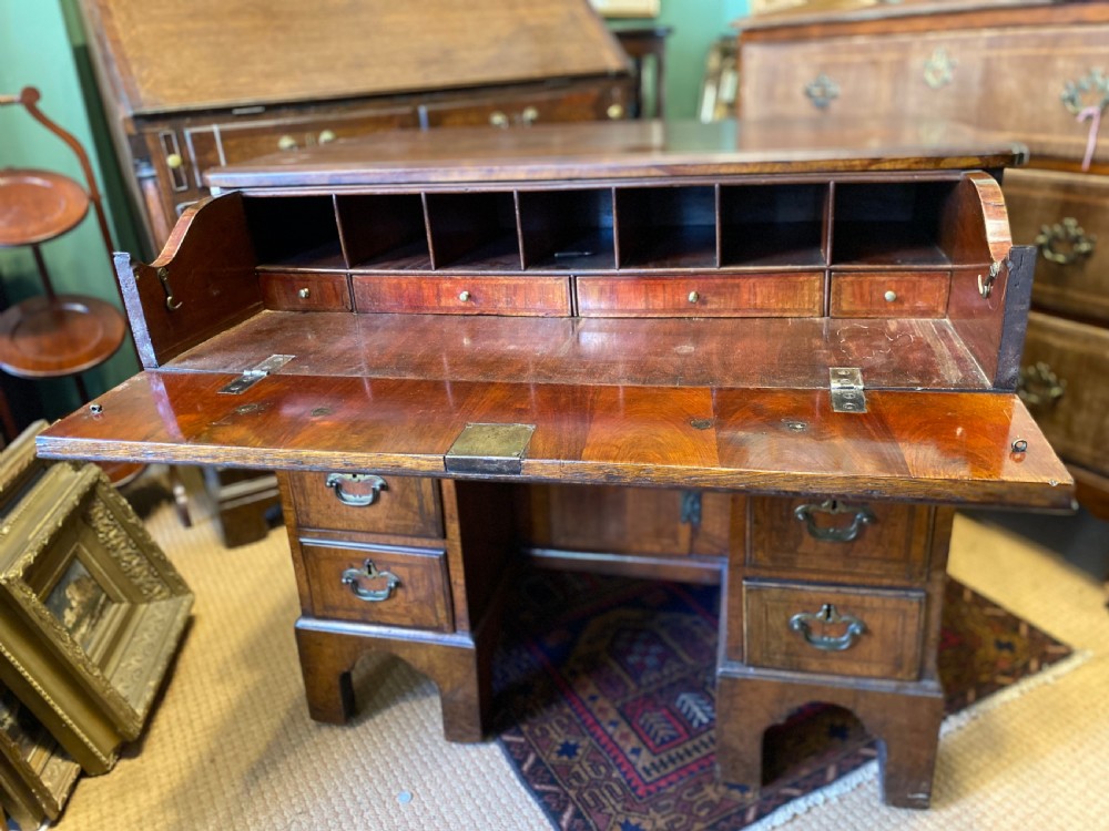 Mid 18th-century walnut kneehole secretaire desk featuring crossbanded drawer fronts, brass drop handles, a central recessed cupboard, and bracket feet. View VI