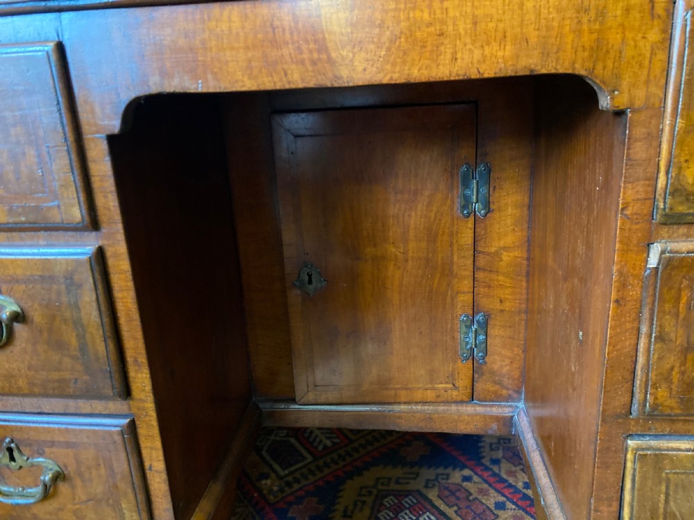 Mid 18th-century walnut kneehole secretaire desk featuring crossbanded drawer fronts, brass drop handles, a central recessed cupboard, and bracket feet. View VII