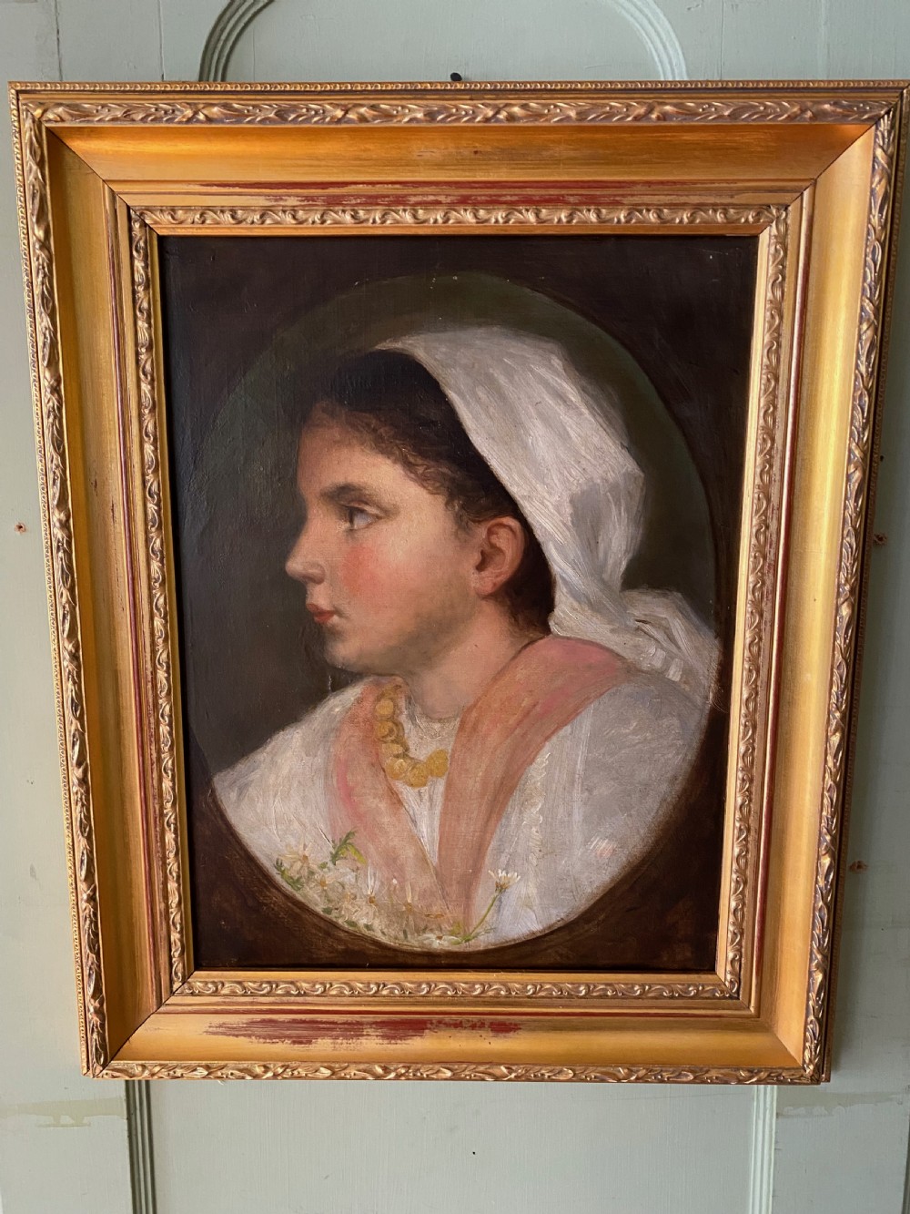 A 19th-century oil portrait depicting the side profile of a young girl wearing a white headscarf, pink shawl, and gold necklace, set within a moulded gilt frame.