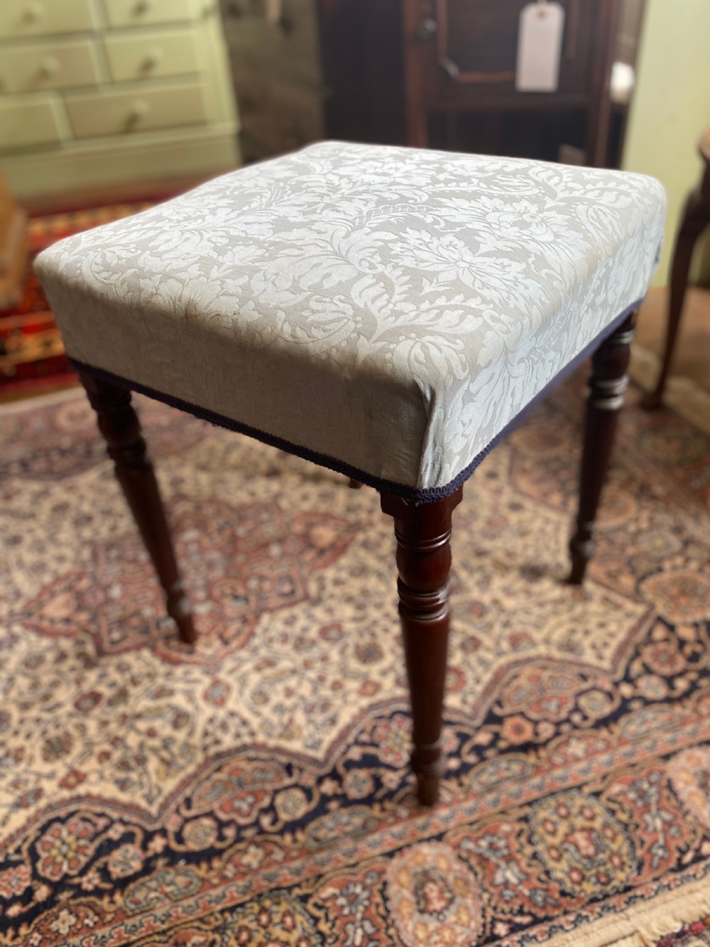 A square Regency stool upholstered in cream patterned fabric with dark turned mahogany legs.