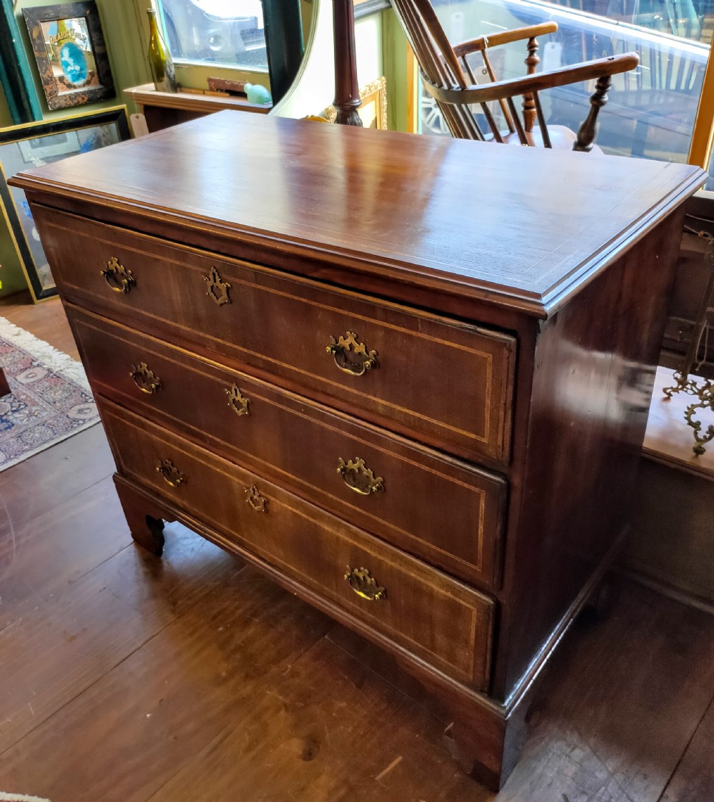 A late eighteenth-century mahogany chest of three drawers featuring fine boxwood stringing inlay, brass swan-neck handles, keyhole escutcheons, and bracket feet. View II