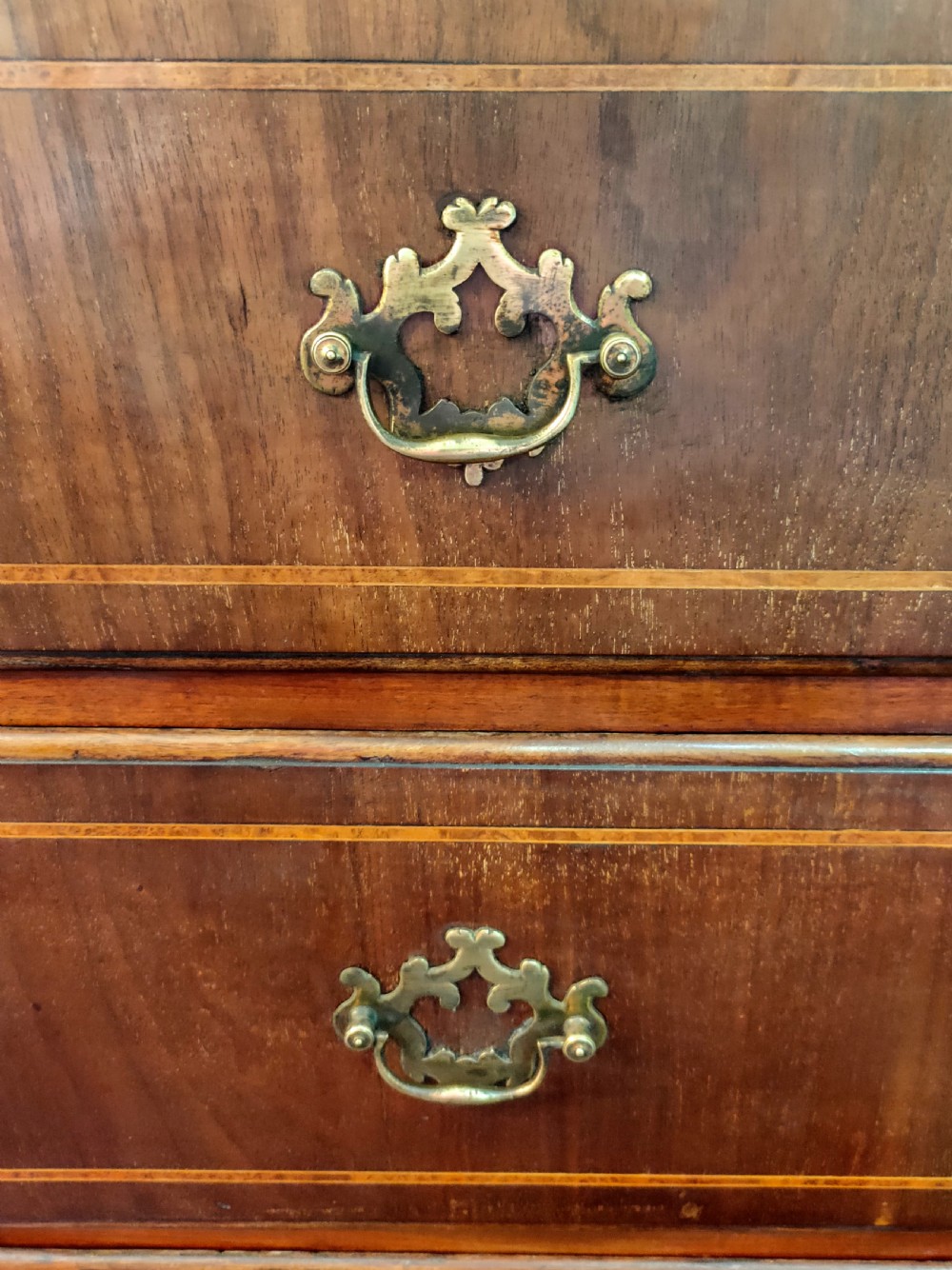 A late eighteenth-century mahogany chest of three drawers featuring fine boxwood stringing inlay, brass swan-neck handles, keyhole escutcheons, and bracket feet. View V