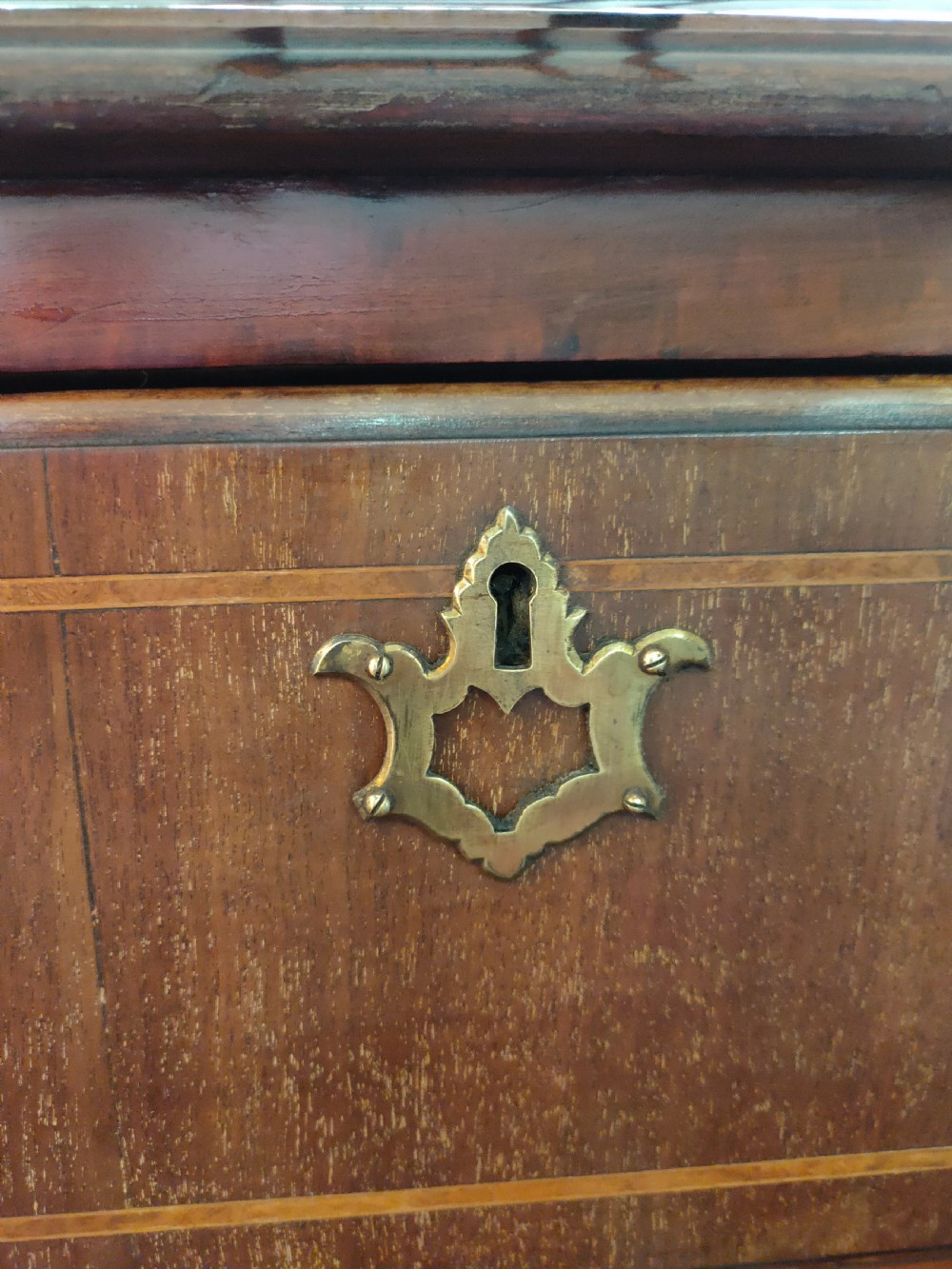 A late eighteenth-century mahogany chest of three drawers featuring fine boxwood stringing inlay, brass swan-neck handles, keyhole escutcheons, and bracket feet. View VI
