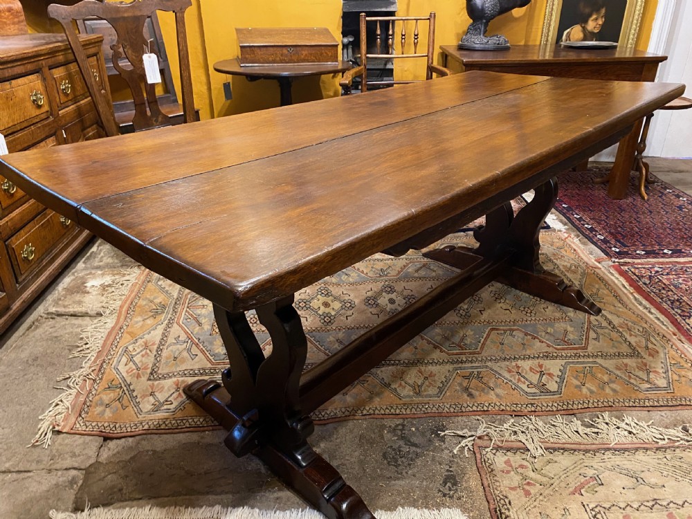An early nineteenth-century solid oak refectory table featuring a two-plank top supported by shaped trestle end supports and a central stretcher.